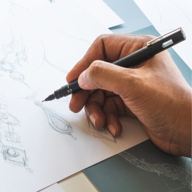 Close-up of a designer's hand finishing a sketch of a bullion concept.