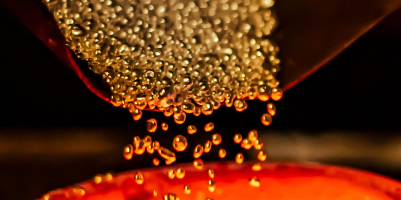 Beads of gold being poured into a melting pot.